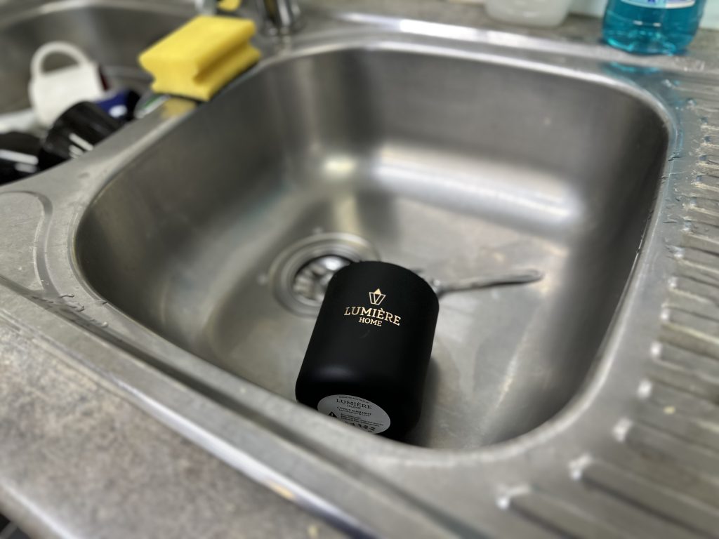 Lumiere black candle jar in the sink with some cutlery. Blurred background of dishes in sink.